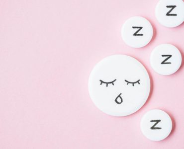 Sleeping pills with Zzzs written on them are shown against a pink background.