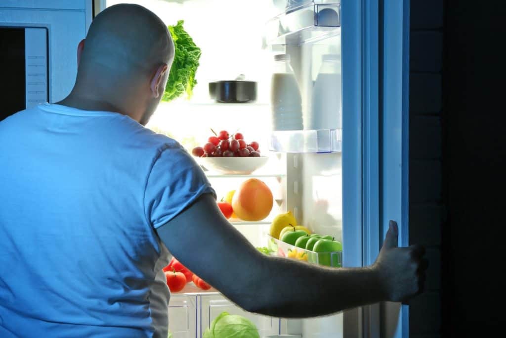 Man stands in front of refrigerator trying to decide what to eat before bed.
