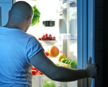 Man stands in front of refrigerator trying to decide what to eat before bed.