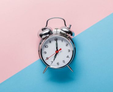 An alarm clock sits against a backgroud representing day and night.