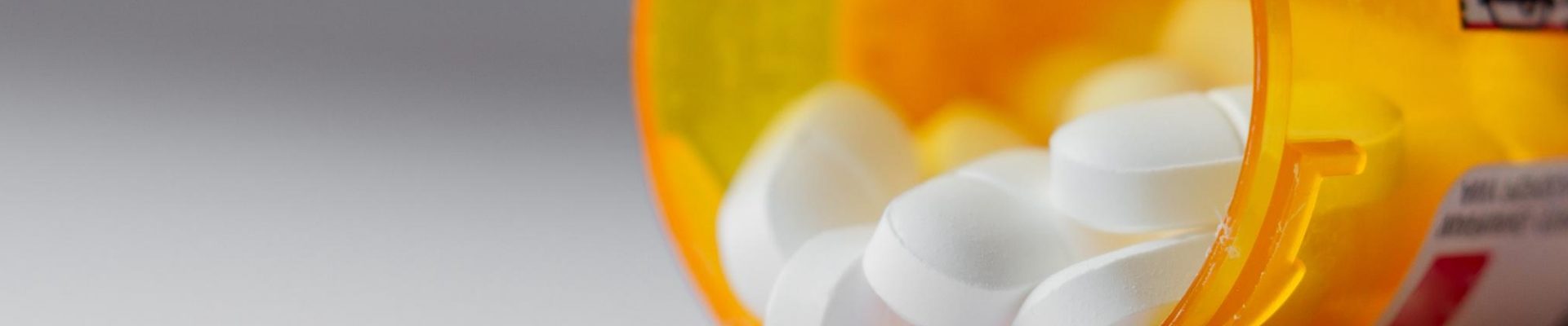 A bottle of prescription opioid pills spilling onto a table.