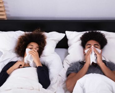 A young couple lies in bed sick and sleepless.