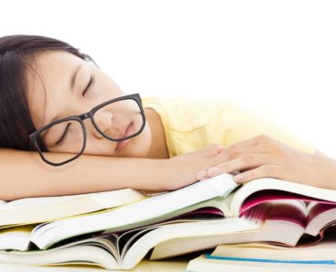A tired student asleep on top of homework books.