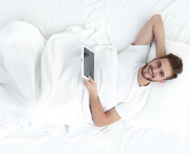 A man relaxes in bed with a tablet.